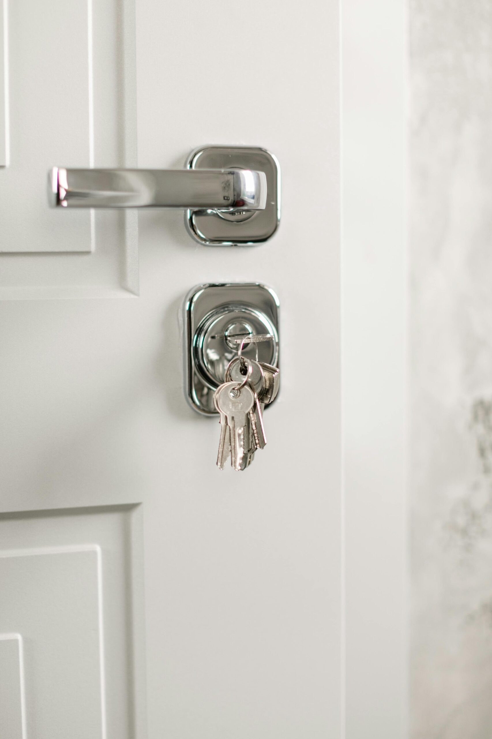 Close-up of a modern chrome door handle and lock on a white door, with a set of keys inserted.