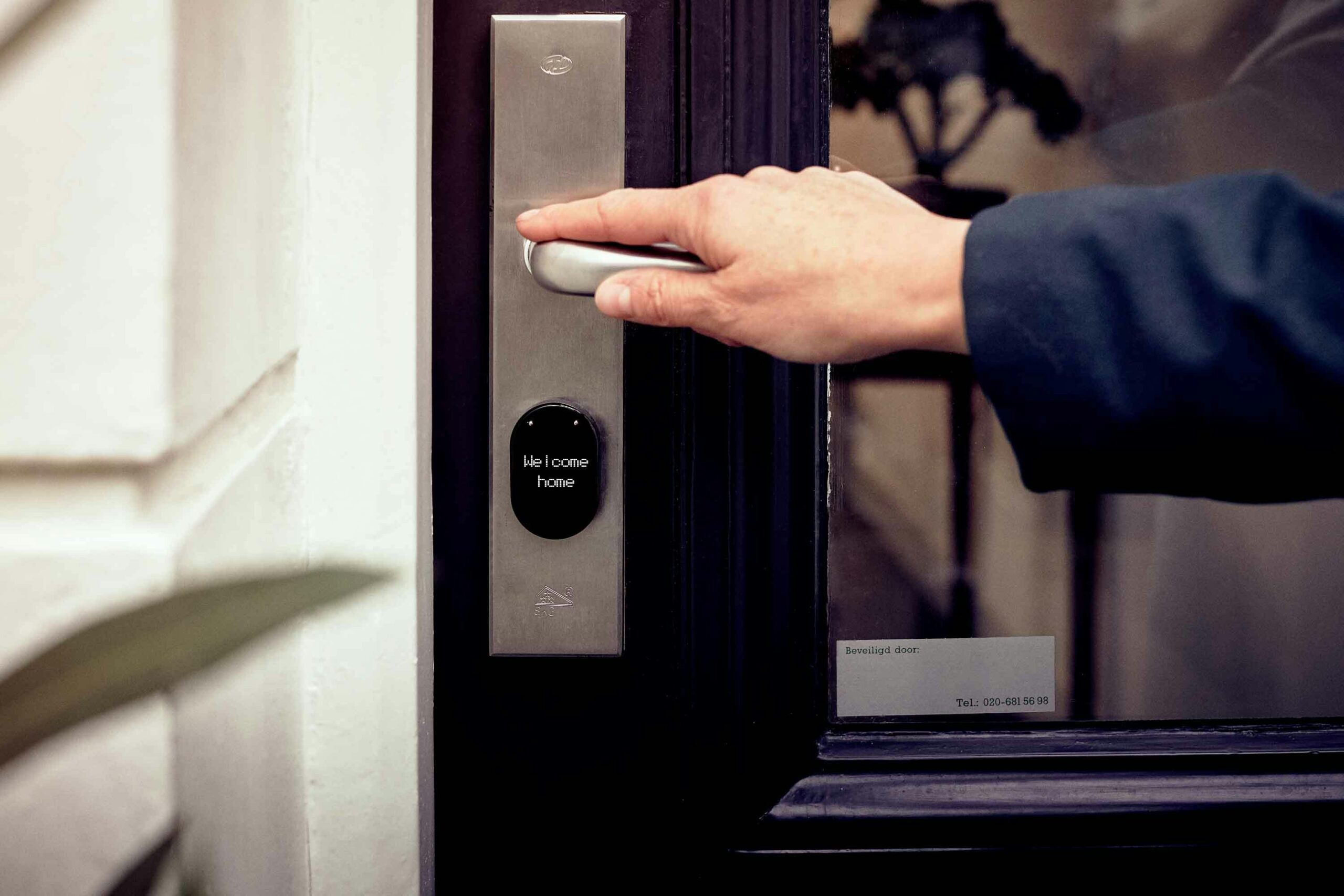 Person unlocking a smart door lock with a digital display that reads “Welcome home,” mounted on a glass entrance.